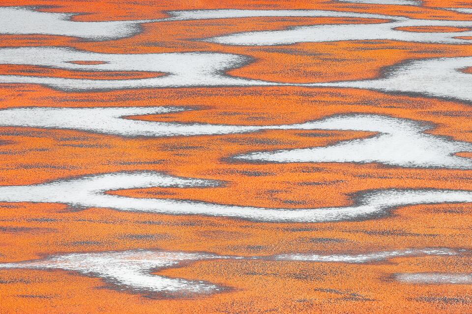 Sunset light reflects on the icy surface of a pond that's striped with white streaks of snow to create an unusual and intriguing abstract composition.