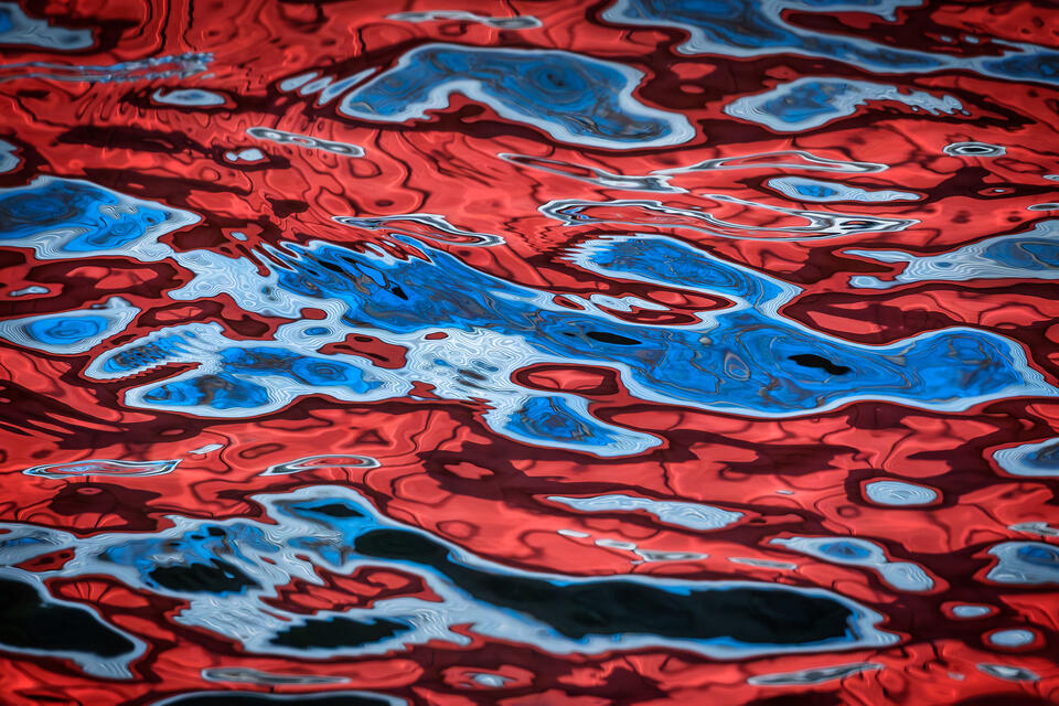 An abstract composition of a red and blue boathouse reflecting on the surface of Lake George in New York's Adirondack Mountains.