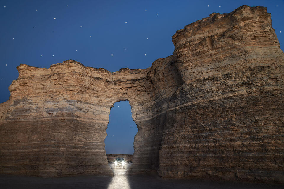 The headlights of a Land Cruiser shine through a keyhole in the beautiful rock formations of Monument Rocks, Kansas, on a clear October night.