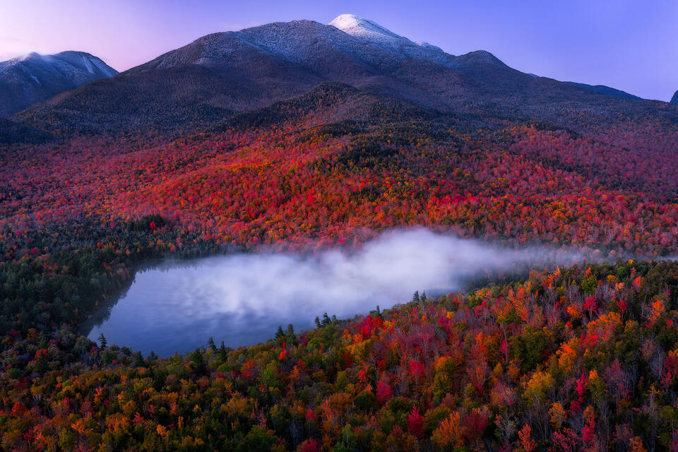 Snow-capped Algonquin Peak is visible as fog drifts off the surface of Heart Lake during peak autumn foliage. 