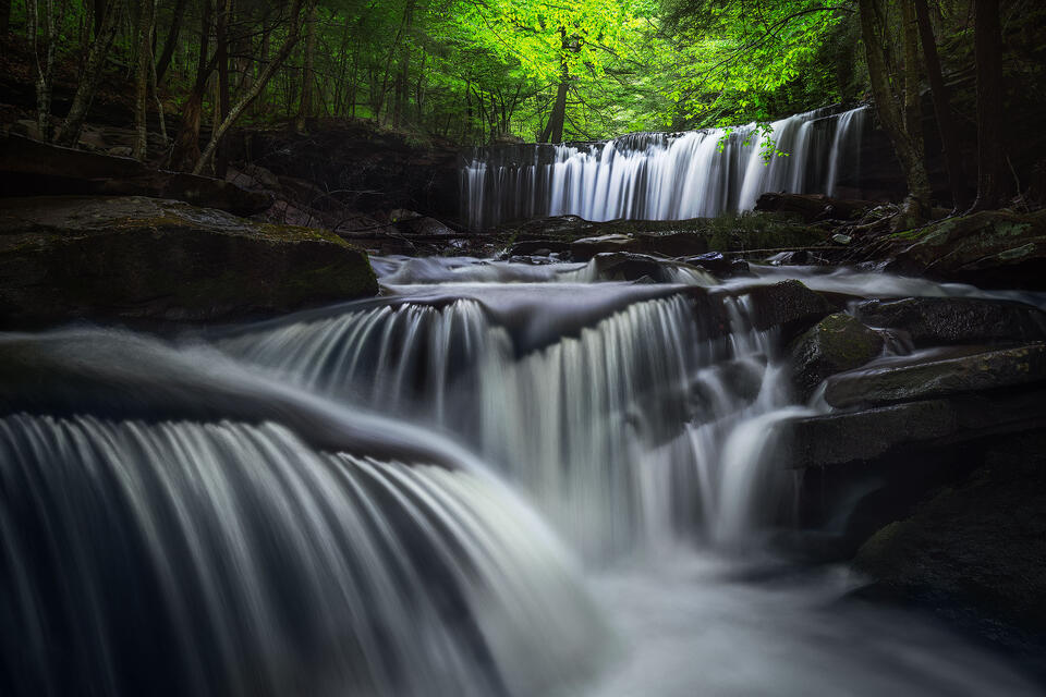 Cascading waterfall spills over rocks below spring foliage in Ricketts Glen State Park. 
