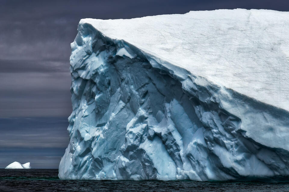 Chiseled face of a large iceberg looks out towards a fellow comrade floating on the horizon.