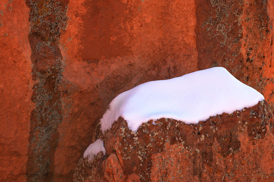 A snowcapped sandstone boulder stands out against a striped sandstone wall after a winter storm.