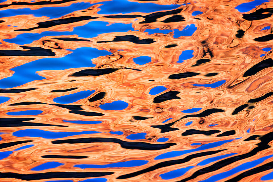 The sunlit walls of Zion Canyon and the clear blue sky reflect in the shadowed surface of a river to create an abstract composition.
